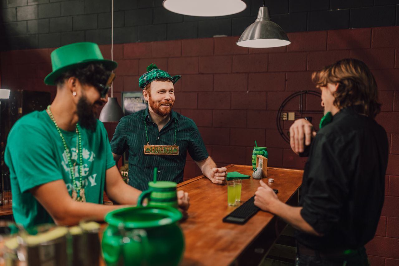 services-img Three men enjoying St. Patrick's Day festivities at a bar, surrounded by green decor.